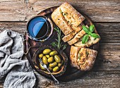 Glass of red wine, green mediterranean olives, freshly baked ciabatta bread in dark wooden plate