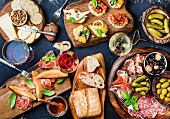 Italienische Antipasti auf Holzbrettern (Brushettas, Käse, Oliven, Gurken, Prosciutto di Parma, Melone, Salami)