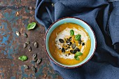 Turquoise ceramic bowl of pumpkin and sweet potato cream soup with fresh basil, cream and seeds
