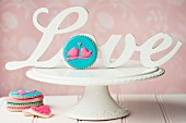 Cookies decorated with pink iced lovebirds, on a white cakestand with vintage love sign