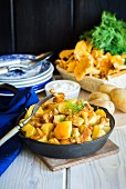 A frying pan with fried potatoes and chanterelle mushrooms