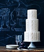A white three-tiered wedding cake with a plaited pattern in front pf a blue background