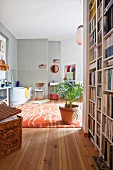 Raumhohes Bücherregal und Korbtruhe im Vorraum, wohnliches Badezimmer mit Zimmerpflanze auf Teppich, Badewanne und hellgrauer Wand