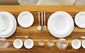White plates, silver cutlery, glasses and bowls ok a wooden table (seen from above)