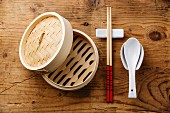 Asiatisches Geschirr mit Bambuskörbchen, Essstäbchen und Keramiklöffel auf Holzuntergrund