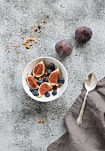 Oat granola crumble with fresh figs and blueberrie in white bowl on grunge grey backdrop