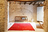 Red rug and wooden bench in foyer of restored stone house