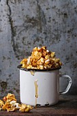 Caramelized sweet popcorn served in vintage enameled white mug with pouring caramel