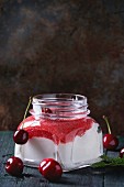 Square glass jar with homemade yogurt with strawberry puree and cherry, served with fresh berries