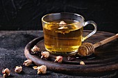 Glass cup of hot herbal tea with dry roses buds, served with honey on honey dipper