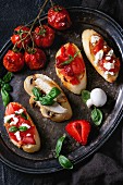 Verschiedene Bruschetta mit Tomaten, Erdbeeren, Feta-Käse, Hähnchen, Champignons und Basilikum auf Vintage Metalltablett