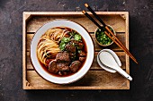 Asian noodles in broth with slow cooked Beef in wooden tray on dark background