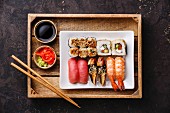 Sushi Set nigiri and rolls with chopsticks, ginger, soy sauce and wasabi in tray on dark background