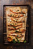 Grilled fried Tiger prawns shrimps on skewers with green sauce and lemon on metal grid baking sheet background
