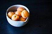 Apricots in a bowl on a dark surface