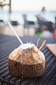 A coconut with the top chopped off containing a straw