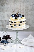 A meringue layer cake with whipped cream, lemon curd and berries on a cake stand