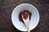 Red peppercorns with a wooden spoon in a bowl (seen from above)