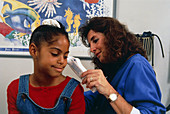 Nurse using digital thermometer in ear of girl