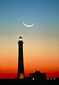 Crescent moon over lighthouse at sunrise