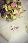 Ring cushion with motto 'SAY YES!' in front of bridal bouquet