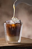 Sweetened condensed milkbeing poured into a glass of Vietnamese iced coffee