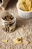 Capers in a glass jar next to crackers