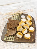 A vegan almond cheese roll cut into slices with a sesame seed crust and crackers