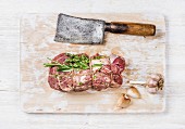 Raw uncooked roastbeef meat cut with rosemary, thyme and garlic and butcher knife on old white painted wooden background