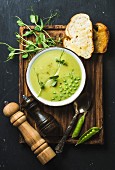 Fresh homemade pea cream soup in white bowl with grilled bread on wooden board