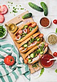 Homemade hot-dogs on wooden serving board with fresh vegetables, spices, ketchup and mustard