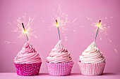 Three cupcakes with pink frosting and sparklers