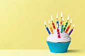Geburtstags-Cupcake mit bunten Kerzen vor gelbem Hintergrund