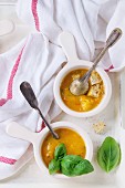 Two small bowls of carrot soup, served with kitchen towel, vintage spoons, fresh basil and croutons