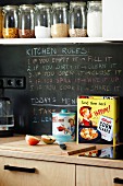 Storage jars on white kitchen shelf above writing on chalkboard splashback and retro tins