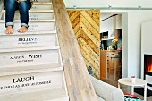 Restored wooden staircase with mottoes on risers and view of fire in stove and kitchen