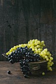 Red and white grapes in an old metal bowl against a wooden background