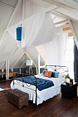 Luftiges Schlafzimmer mit Dachkonstruktion und weißer Stoffbahn über Metallbett