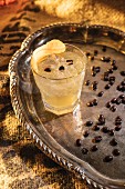 A mezcal drink on a silver tray with coffee beans