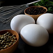An arrangement of eggs, peppercorns and a whisk (close-up)