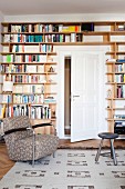 Bücherwand mit integrierter weißer Zimmertür, davor gemütlicher Armlehnsessel