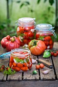 Eingelegte und frische Tomaten mit Zutaten auf Holzkiste im Garten