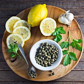 Lemons, capers, garlic and parsley on a wooden plate