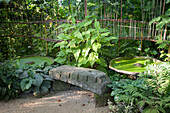 Stone bench and pool covered in duckweed below wooden artwork