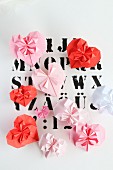 Origami hearts in pin and red on paper printed with letters