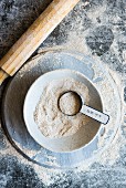 Spelt flour in a bowl with a measuring spoon next to a rolling pin