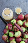 Fresh naturally cloudy apple juice in a glass and bottlenecks to a basket of apples