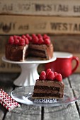Sliced chocolate cake with raspberries on a cake stand and plate