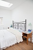 Black metal bed and wooden bedside cabinet in pale bedroom