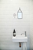 Sink below small mirror next to motto on white tiled wall